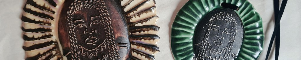 detail of 2 small round ceramic medallions with portraits of black girl in braids embossed on them and frame of ridged rays. Black, green and cream glazes.